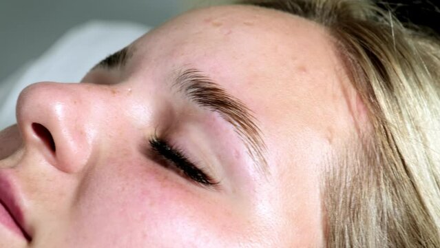 Blonde woman lies waiting for eyebrow lamination procedure in beauty room. Female client with closed eyes enjoys modern salon service closeup