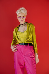 tattooed albino model in stylish outfit and sunglasses posing on carmine pink.