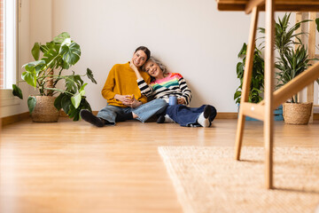 Smiling mother and daughter sitting on hardwood floor at home