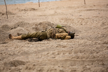 Historical reconstruction. Injured or dead World War II infantry  soldier  on the beach. View from the back.  Hel, Poland - obrazy, fototapety, plakaty