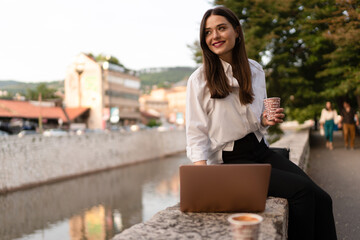 Fototapeta premium The woman works outside on the laptop and drinks coffee 