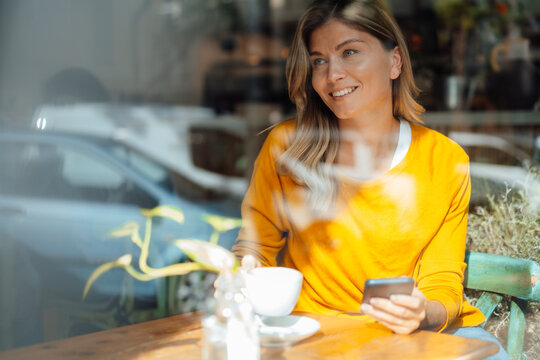 Happy woman having coffee in cafe seen through glass