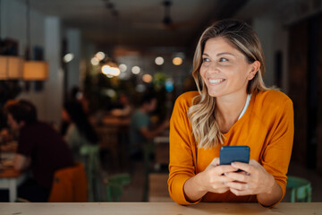 Thoughtful happy woman with smart phone sitting in cafe