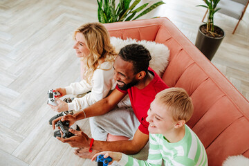 Friends with game controller playing video game sitting on sofa at home