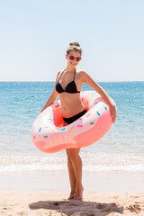 Naklejka na ściany i meble Young sexy pretty woman stay on the sea beach and play with inflatable ring donut and has fun. Summer holidays and vacation concept