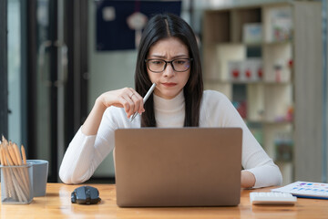 Concerned female worker looking at laptop screen suspiciously, thinking about problem-solving,...
