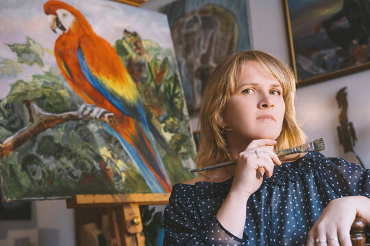 Painter holding paintbrush in front of bird painting