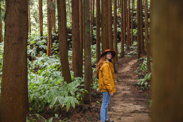 Redhead woman wearing hat standing amidst tall trees in forest