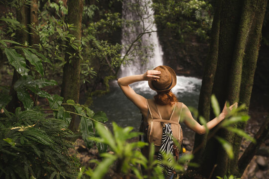 Young woman wearing hat standing in front of waterfall