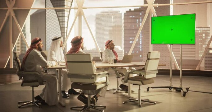 Group of Middle Eastern Executives and Management Having Conference Video Call with a Remote International Office. Businessmen Watching a Presentation on TV with Green Screen Mock Up Display.