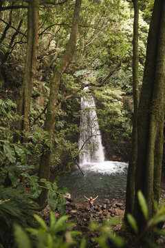 Woman with arms raised standing in front of waterfall