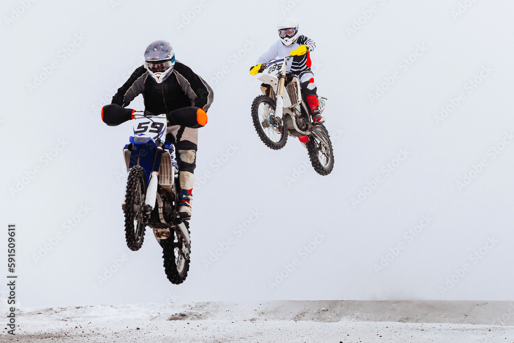 Wall mural two motorsport rider jumping together on snowy springboard, winter off-road motorcycle racing