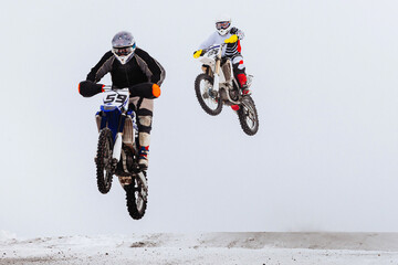 two motorsport rider jumping together on snowy springboard, winter off-road motorcycle racing
