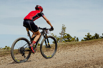 cross-country cycling, athlete cyclist riding mountain bike uphill on gravel road