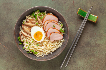 Japanese ramen noodles with pork slice, shiitake mushrooms and egg in a black bowl. Top view