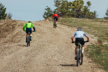 rear view three mountainbikers riding bike uphill, biking on gravel road, cycling competition