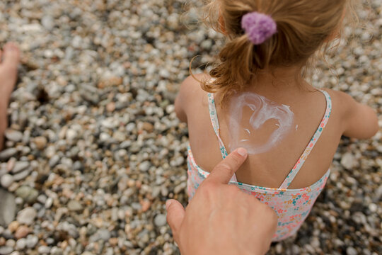 Man drawing heart shape with suntan lotion on daughter at beach