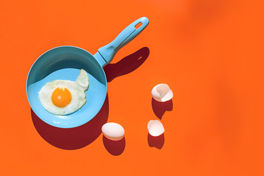 Frying pan with eggs placed against orange background