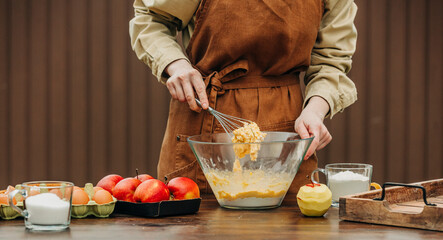 Woman in apron stirring cake dough in mixing bowl at table