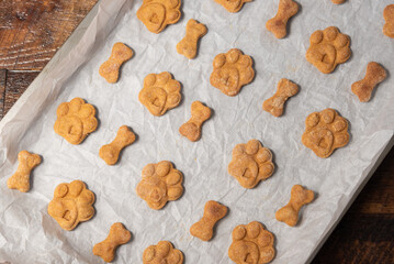 Rows of bone and paw print shaped dog treats on a parchment paper lined baking pan.
