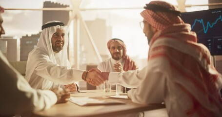 Middle Eastern Business Partners Striking a Successful Deal at a Corporate Modern Meeting Room. Two Arab Men Shaking Hands, Managers in Traditional White Robes Celebrating and Clapping Hands
