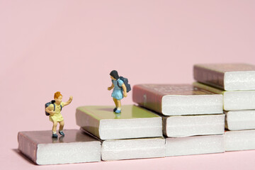 Miniature tiny people toy photography. Two girl students with school backpack standing above book stair. Isolated on pink background.