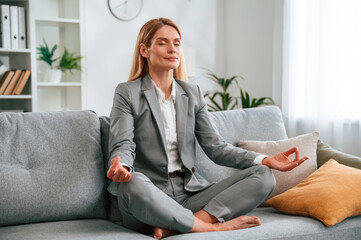 Lotus pose, meditation. Woman in formal clothes is at home, sitting on the sofa