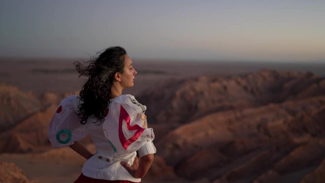 rear view young latin woman standing at the viewpoint over the valley of the moon at sunset looking at the horizon and desert landscape