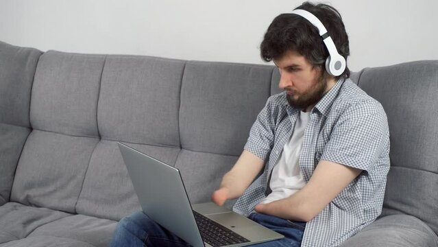 Disabled man with amputated two stump hands in headphones is listening music on laptop at home sitting on sofa. Problem of adaptation to life people with disabilities. Independent Invalid person.