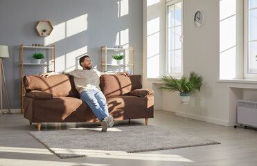 Happy house owner relaxing on comfortable sofa at home. Man enjoying leisure time and sitting on...