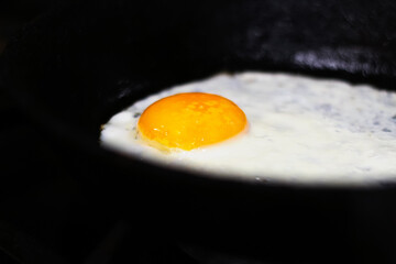 Fried egg on frying pan. Black night. One fried egg in cast iron frying pan sprinkled with ground black pepper. Out of focus