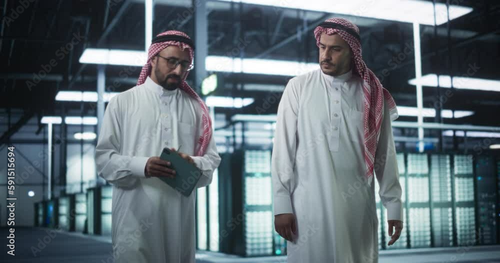 Poster In the Modern Data Center: Middle Eastern Engineer and IT Specialist Working in Server Room, Talking, Doing System Maintenance Check with Tablet Computer. Specialists Doing Database Diagnostics