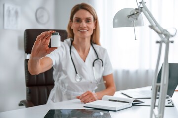 Holding pills. Young female doctor in white coat is indoors