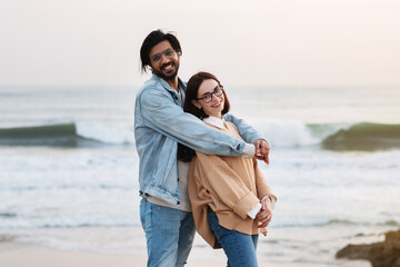 Weekend together. Cheerful millennial indian husband hugging caucasian wife in cagual outdoor, enjoy love