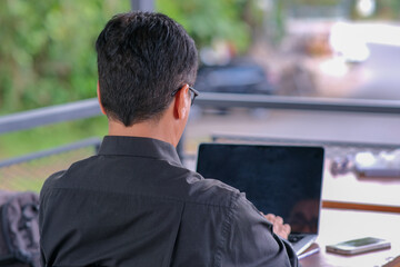 Back view: A middle-aged man is working on his laptop.