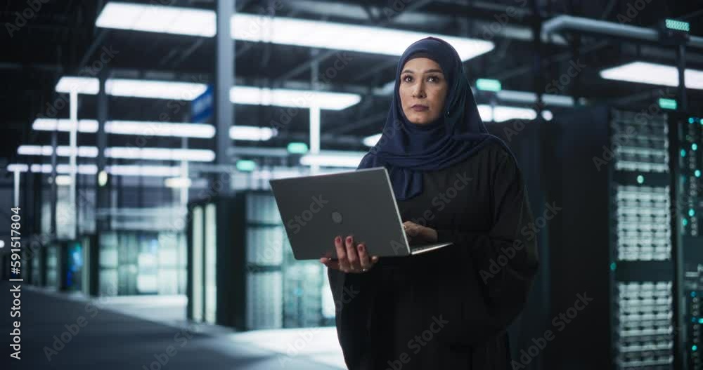 Poster Muslim Female Data Center IT Engineer Standing in a Room with Server Racks. Cloud Computing Architect Uses Laptop Computer for Servicing the System in Cyber Security and Data Protection Facility