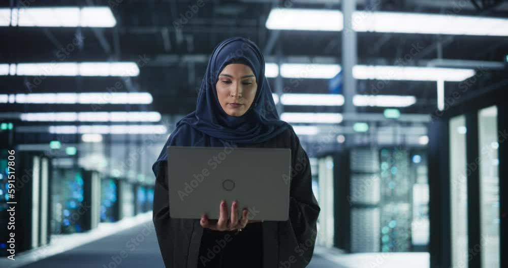 Poster portrait of a young middle eastern female it system engineer wearing traditional hijab, using laptop
