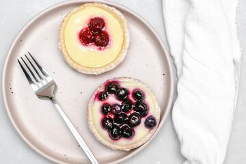 Delicious red raspberry strawberry, blueberry whipped creamy tartlets,cakes.gourmet confection dessert on plate with napkin.sweet tasty pastry baked pie cheesecake with ripe berries on gray table