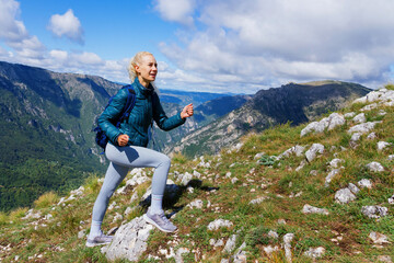 Naklejka na ściany i meble A joyful young woman while climbing in the mountains. Active recreation and tourism