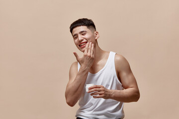 Portrait of smiling, handsome, young guy with clean, spotless face applying face moisturizing cream...