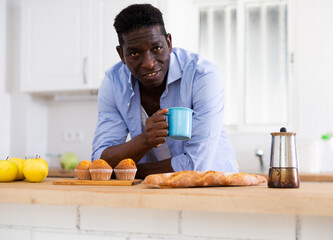 African american man eating sweet cupcakes in kitchen during breakfast