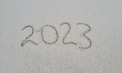 Drawn numbers 2023 on sand are washed away by sea wave