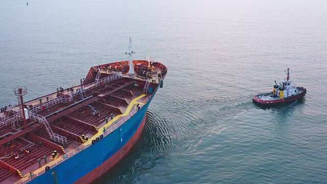 Close up Tugboat drag cargo ship near sea port aerial view. Maritime navigation and cargo transportation by sea