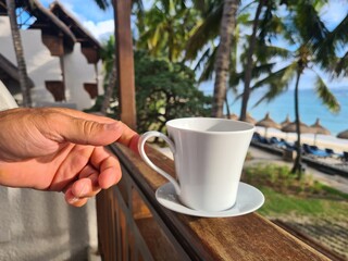 White coffee mug in man hand on terrace overlooking sea or ocean