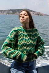 Fototapeta premium Young woman in knitted sweater standing on yacht with sea and Princess islands at background in Turkey.
