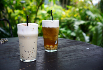 Lotus seed ice tea and creamy milk tea glassed on wood table in background of green garden         ...