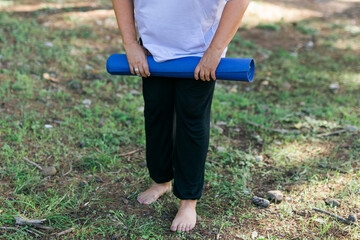 Portrait of mature elderly woman with grey hair dreadlocks going to workout in park and standing with mat for exercises against sea