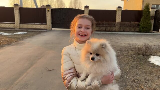 a girl walks with a dog, holds it in her arms and smiles, a teenage girl in a jacket holds a small spitz in her arms, taking care of pets