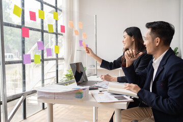 Happy young Asian businessman and woman shaking hands to congratulate successful collaboration on business deal with documents and laptop on table in the office.