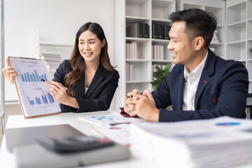 Happy young Asian businessman and woman shaking hands to congratulate successful collaboration on business deal with documents and laptop on table in the office.